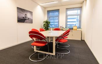 Contemporary office space rental at Siriusdreef 17, Hoofddorp, with a round meeting table and vibrant red chairs.