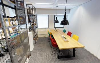 Bright office space at Meidoornkade 22, Houten, featuring a long wooden table with colorful chairs, ideal for meetings. Shelves line one wall, adding functional storage.