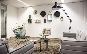 Furnished office space for rent featuring stylish gray sofas, a standing lamp, and decorative wall items, located at Meidoornkade 22, Houten.