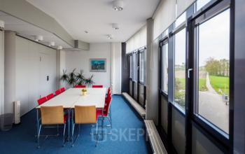 Bright meeting room with a long table and red chairs in an office space rental at Eurodepark 1, Kerkrade.