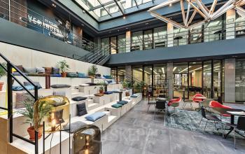 Modern office space at Tunisstraße 19-23, Cologne Center, featuring a spacious, well-lit atrium with seating arrangements, decor, and plants for a welcoming work environment.