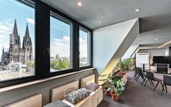 Modern conference room with large windows in Cologne Center's Tunisstraße 19-23, showcasing a stunning view of Cologne Cathedral. Office space rental with stylish seating and presentation setup.