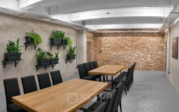 Nowoczesne powierzchnie biurowe na wynajem w Krakowie przy Przemyslowa 12 z drewnianymi stołami i komfortowymi krzesłami, otoczone zielonymi roślinami i ceglaną ścianą