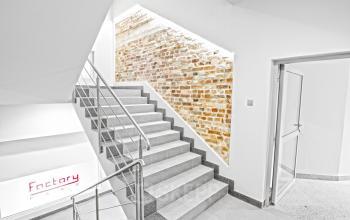 Nowoczesne biura na wynajem widoczne na przestrzennym korytarzu z ceglaną ścianą i metalowymi schodami w biurowcu przy Przemysłowej 12 w Krakowie.