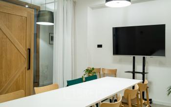 Nowocześnie zaprojektowana przestrzeń biurowa w Krakowie przy Przemyslowa 12, idealna do wynajęcia dla profesjonalistów, ze stylowymi drewnianymi meblami i dużym monitorowym TV na ścianie.