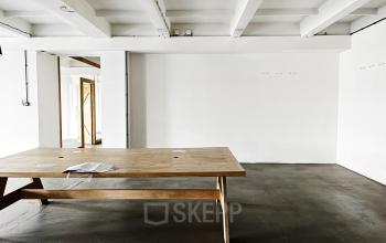 Widok na przestronne i nowoczesne powierzchnie biurowe na wynajem przy Przemyslowa 12 w Krakowie z dużym drewnianym stołem w centrum.