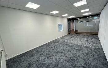 A modern, unfurnished office interior at Industriepark 5B in Leek, showcasing a spacious layout perfect for office space rental. The room features carpet flooring, white walls, and fluorescent lighting.