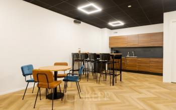 Modern office kitchenette at Industriepark 5B in Leek, featuring stylish wooden cabinets, a long counter with bar stools, and a seating area with chairs around a small table. Ideal for office space rental.