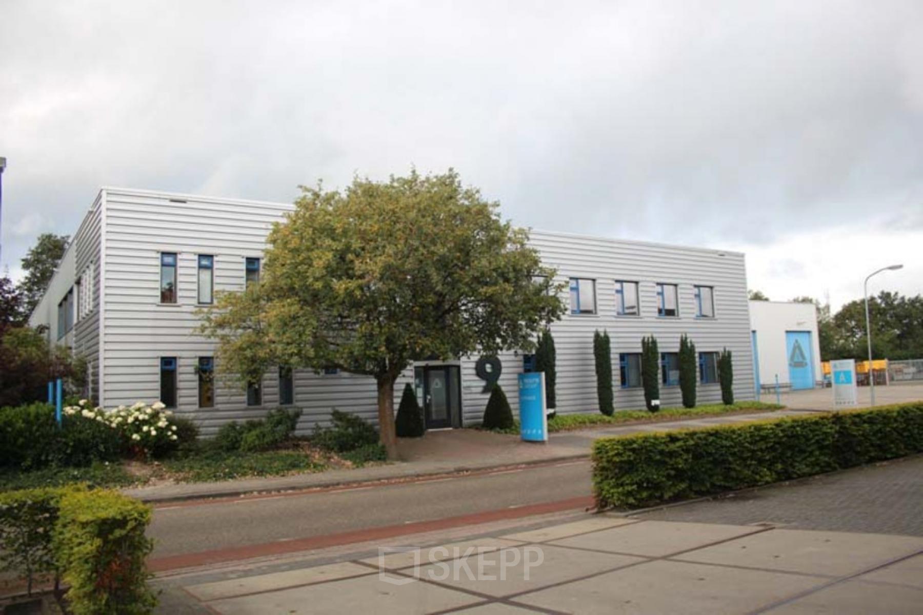 Exterior view of the office building at Industriepark 9, Leek, showcasing a modern facade surrounded by greenery, perfect for office space rental.