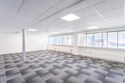 Spacious and bright office space rental at Ouddeelstraat 7a, Leeuwarden, featuring large windows for natural light and modern carpeting, ideal for various professional activities.