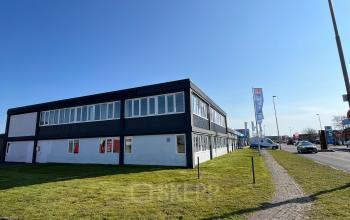 Exterior view of the office building at Zwettestraat 15, Leeuwarden, showcasing a modern design perfect for office space rental. The building is surrounded by a green lawn under a clear blue sky.