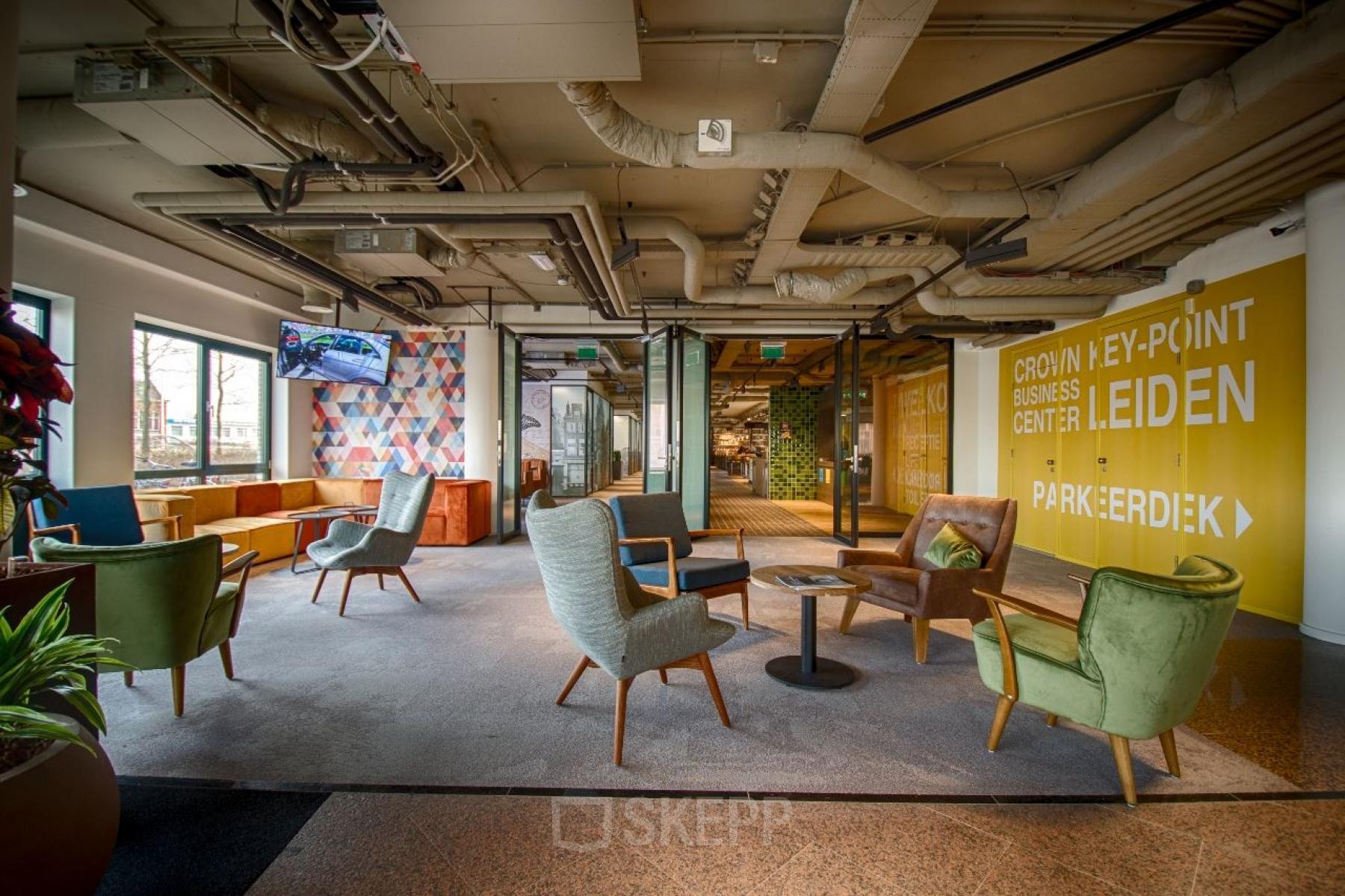 Modern lounge area with colorful seating and large windows at Schipholweg 103, Leiden, ideal for office space rental.
