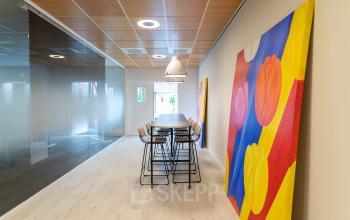 Bright office space in Leiden at Pompoenweg 3 - 15 with colorful wall art, high chairs around a long table, and modern lighting, available for office space rental.