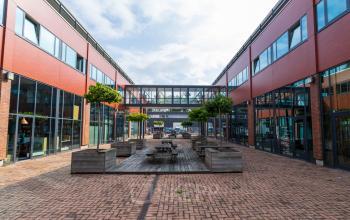 Courtyard view of office building at Pompoenweg 3 - 15, Leiden, with seating and trees lining the pathway.