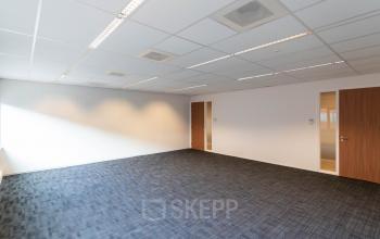 Spacious office to rent at Pompoenweg 3-15 in Leiden, featuring ample natural light and dark carpet flooring, suitable for various business setups.