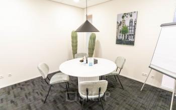 Small conference room at Pompoenweg 3 - 15, in Leiden, with a round table surrounded by four chairs, a flip chart, and minimalistic decor.