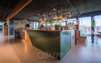 Modern office interior at Bargelaan 200, Leiden, featuring a stylish kitchen area with green tiling, bar stools, and ample natural light.