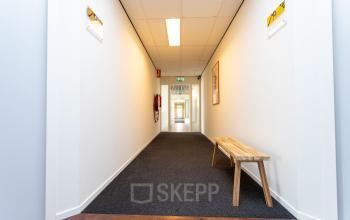 View of a well-lit hallway at Fruitweg 22, Leiden, featuring a wooden bench and bright walls, perfect for office space rental needs.