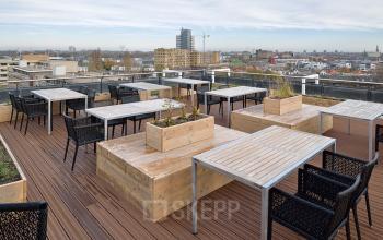 Outdoor rooftop office space rental at Schipholweg 55-89, Leiden, featuring wooden tables and chairs on a deck with panoramic city views.