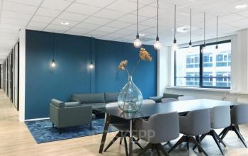 Modern furnished office to rent at Schipholweg 55-89, Leiden with a meeting table, chairs, and a lounge area with sofas and stylish lighting.