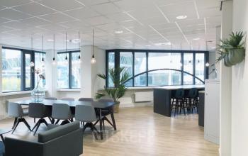 Bright office space at Schipholweg 55-89 in Leiden with modern furnishings, large windows, and a communal table and high stools.