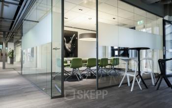 Modern office space to rent at Kanaalpark 140, Leiden, featuring a glass-walled conference room with green chairs and a table.