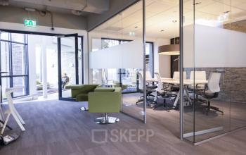 Modern office space rental at Kanaalpark 140 in Leiden with glass-walled meeting room, green lounge chairs, and desk chairs around a conference table.