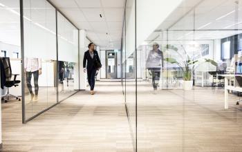 Modern office interior at Kanaalpark 140, Leiden, with glass walls, visible workspaces, and people walking.