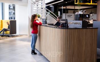 Reception area of an office building at Kanaalpark 140, Leiden, featuring a wooden reception desk with a person standing and another seated at the desk.