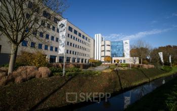 Modern office building at Kanaalpark 140 in Leiden with large windows, surrounded by greenery and flags, offering office space rental.