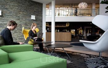 Modern office lounge area at Kanaalpark 140 in Leiden with comfortable seating and individuals working on laptops, ideal for office space rental.