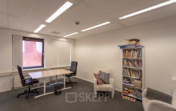 Well-lit office space rental at Kanaalpark 157, Leiden, with a neat desk, comfortable seating area, and a bookshelf.