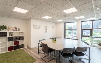 Well-lit office space rental at Kanaalpark 157, Leiden, featuring a large meeting table, comfortable seating, and storage shelves.
