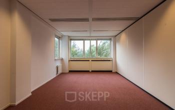 Interior view of a furnished office space available for rent at Vlietweg 17, Leidschendam, featuring large windows and carpeted floors.