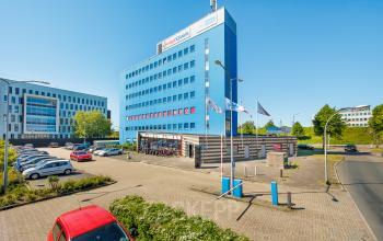 Exterior view of the Het Ravelijn 1-11 office building in Lelystad, featuring a blue multi-story facade with adjacent parking area. Ideal office to rent for modern businesses seeking a strategic location.
