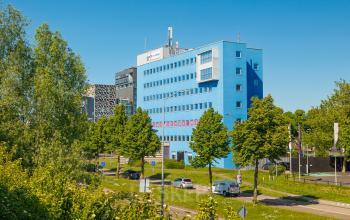 Exterior view of a blue office building at Het Ravelijn 1-11, Lelystad, surrounded by trees and parking. Ideal location for office space rental with ample natural light.