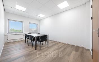 This office space at Het Ravelijn 1-11 in Lelystad features a bright, minimal design with wooden flooring and a table with chairs, ideal for small meetings or workplace activities. Office space rental available.