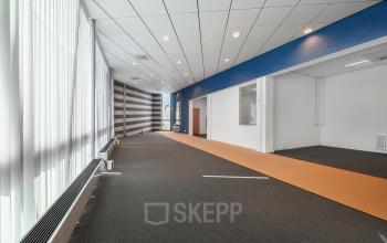Spacious corridor in Het Ravelijn 1-11, Lelystad, with carpeted floors and large windows allowing natural light. Ideal for businesses seeking office space rental with open layout potential.