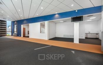 Spacious open floor plan with blue accent wall and carpeted flooring at Het Ravelijn 1-11, perfect for office space rental. Bright windows enhance the modern look of this professional environment.