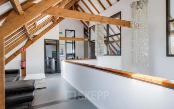 Interior of an office at Hamersveldseweg 120, Leusden, featuring wooden beams, modern furnishings, and decorative lighting. A sleek corridor connects different areas, ideal for office space rental.