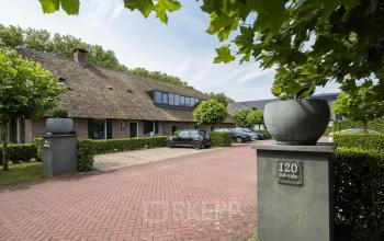 Exterior view of a charming office building with thatched roof at Hamersveldseweg 120, Leusden, perfect for those seeking office space rental. A small parking area is visible in the foreground.
