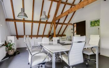 Modern office with exposed beams and sleek furnishings at Hamersveldseweg 120, Leusden, available for office space rental. Spacious seating setup for collaborative meetings.
