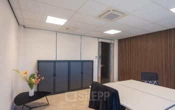 A modern office space at Horsterweg 24 in Maastricht-Airport features a minimalistic design with a large table, chairs, and a small side table with decorative plants. Ideal for office space rental.