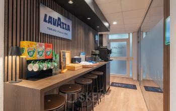 Modern office pantry in Maastricht-Airport featuring a coffee station with stools, a variety of snacks, and Lavazza branding. Ideal for relaxing breaks during office space rental.