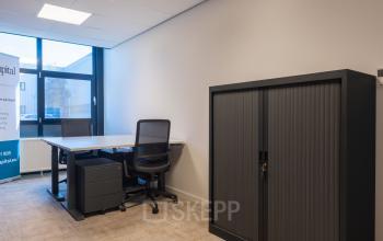 Office space at Horsterweg 24, Maastricht-Airport featuring a desk, chair, and storage cabinet under fluorescent lighting, ideal for workspaces. Suitable for office space rental.
