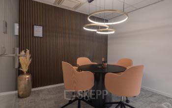 Modern conference room with round table and four peach chairs at Horsterweg 24, ideal for office space rental. Elegant lighting and decorative wall paneling create a stylish meeting environment.