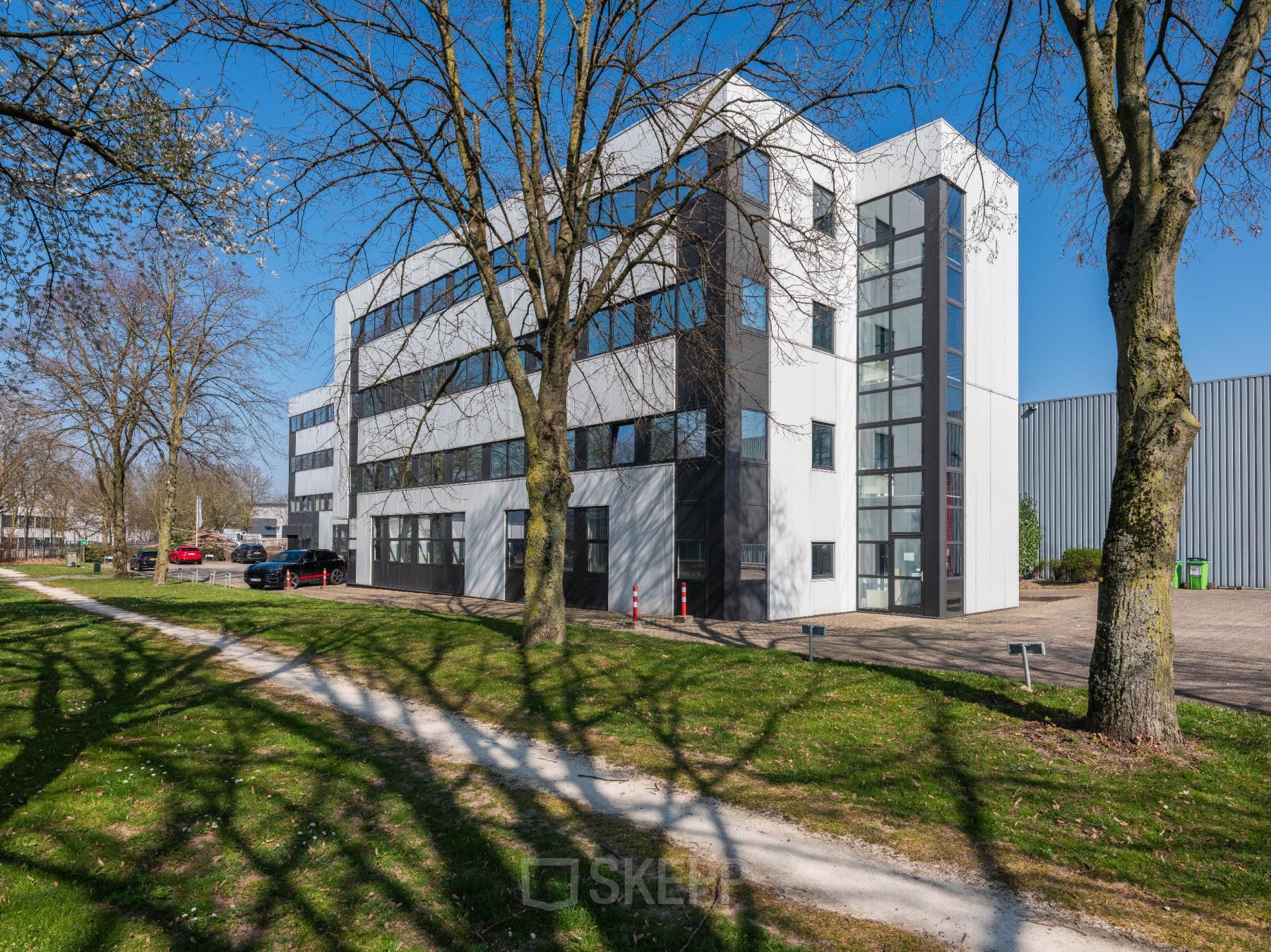 Exterior view of a modern office building at Horsterweg 24, Maastricht-Airport, ideal for office space rental, surrounded by trees and grass.