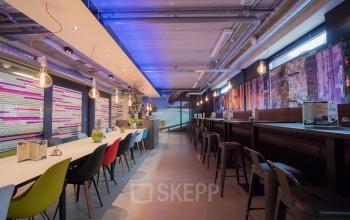 Workspaces at Europalaan 24, Maastricht-Airport with colorful chairs, long tables, and hanging lamps in a modern office setting.