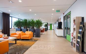 Modern office space rental at Europalaan 24, Maastricht-Airport with bright orange chairs, potted plants, and hardwood flooring.