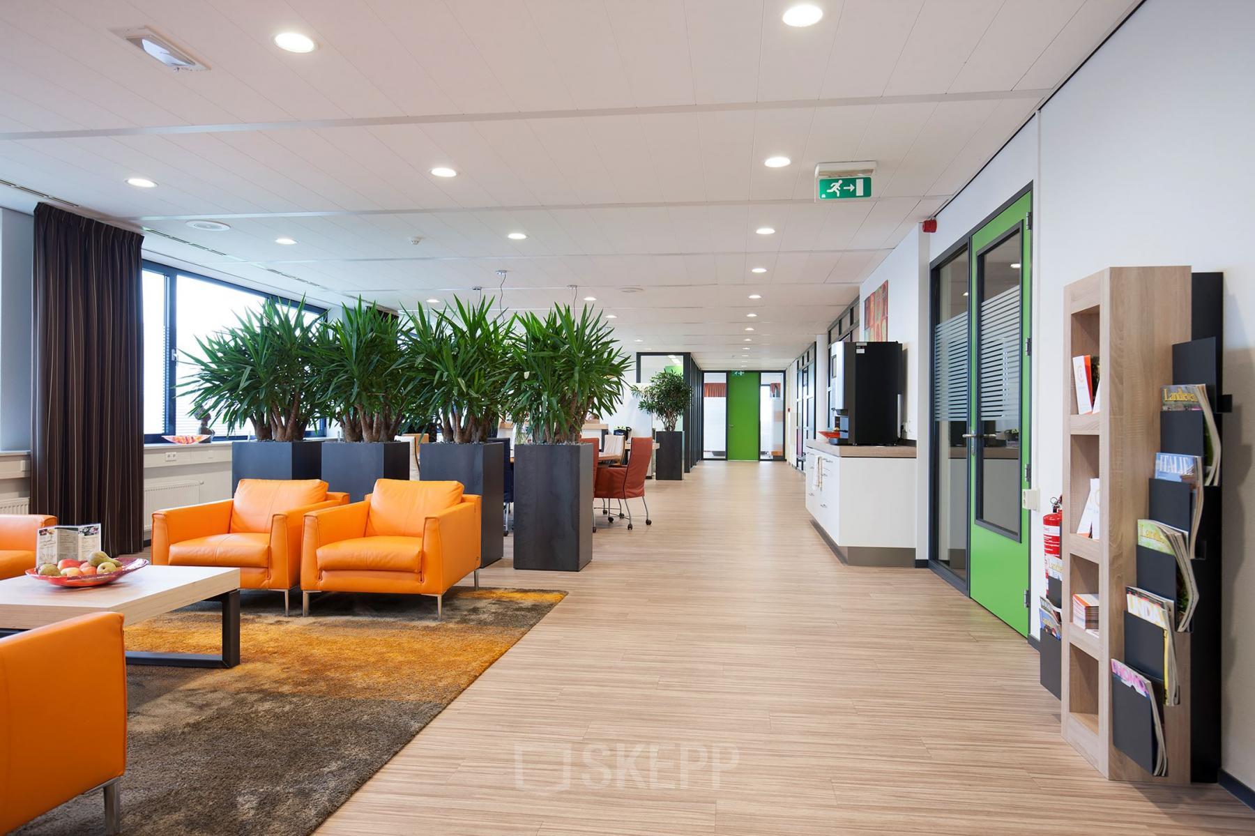 Modern office space rental at Europalaan 24, Maastricht-Airport with bright orange chairs, potted plants, and hardwood flooring.